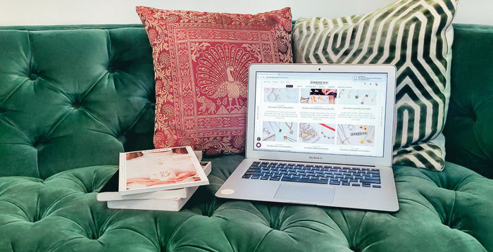 Laptop on a green couch with magazines and pillows next to it.
